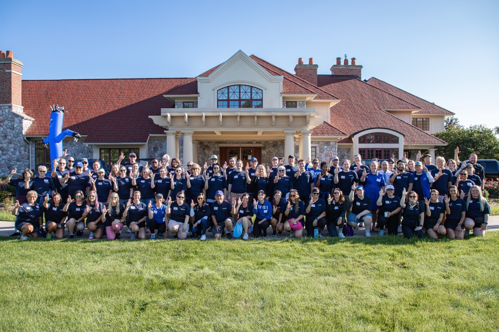 Group of GVSU Alumni Move in day volunteers take a group picture in front of Alumni House and Visitors Center and anchor up